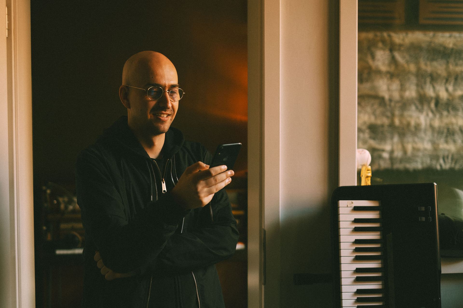 Chriskey lacht entspannt im Studio, Handy in der Hand.